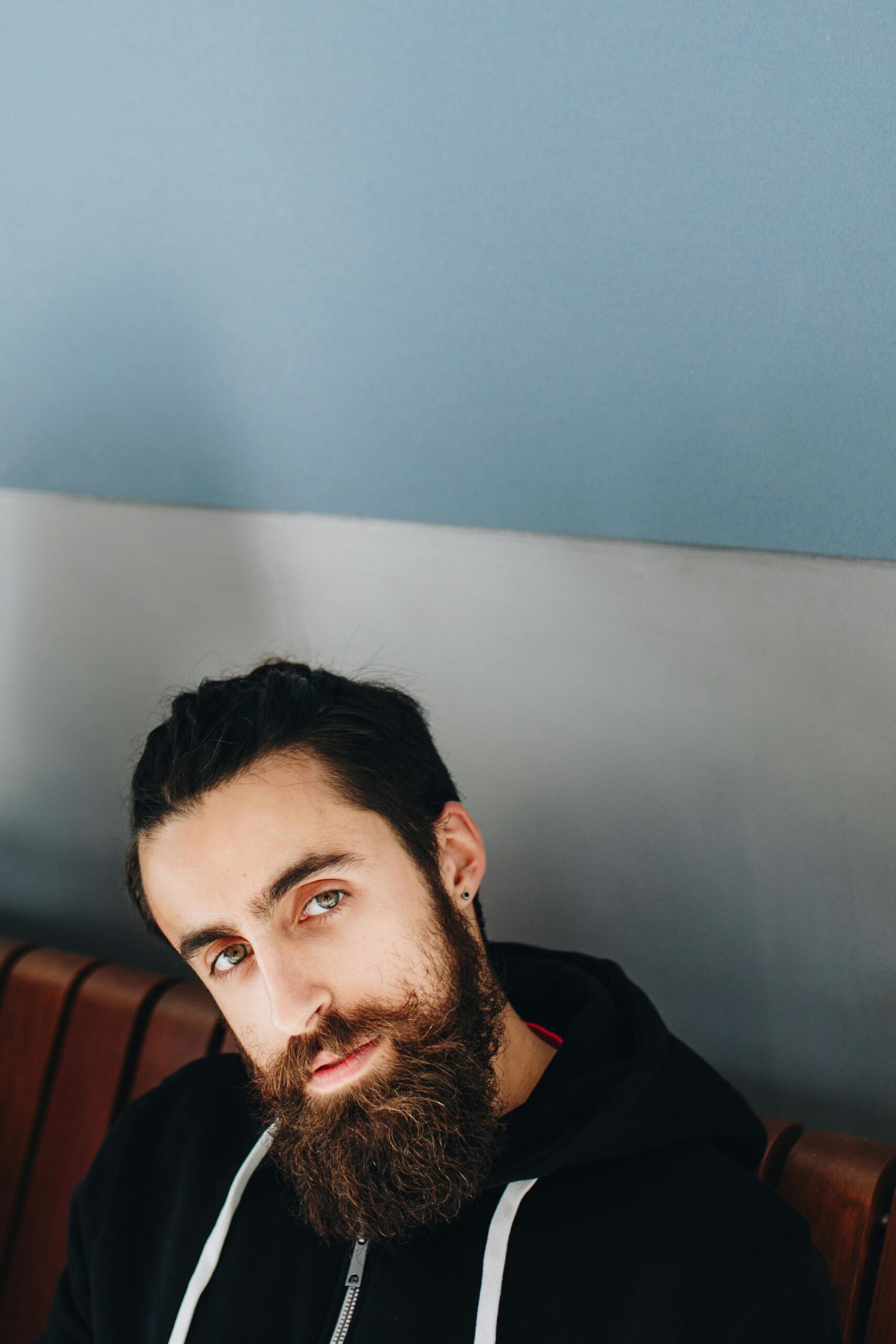 Close-up portrait of a bearded man with green eyes posing indoors against a blue wall.