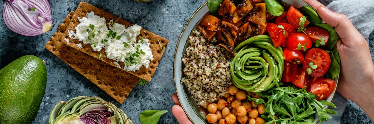 Hands holding healthy superbowl or Buddha bowl with salad, sweet potatoes, chickpeas, quinoa, tomatoes, arugula, avocado on light blue background. Healthy vegan food, clean eating, top view